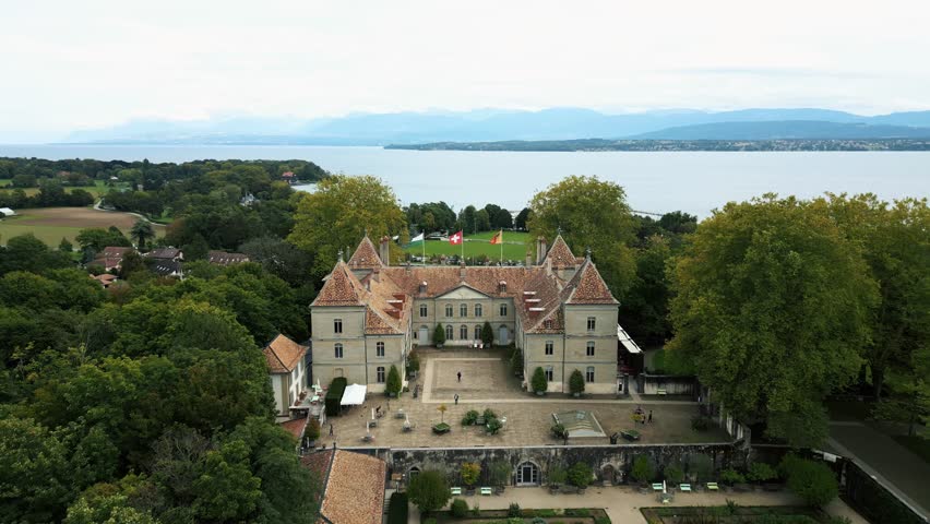 Aerial view of the Château de Prangins with its orange rooftop, surrounded by green trees, overlooking the lake, Prangins, Vaud, Switzerland.