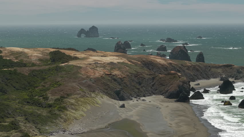 Drone flight over dunes near Crook Point at the Oregon Coast in windy conditions. Mack arch and other sea stacks in the distance.