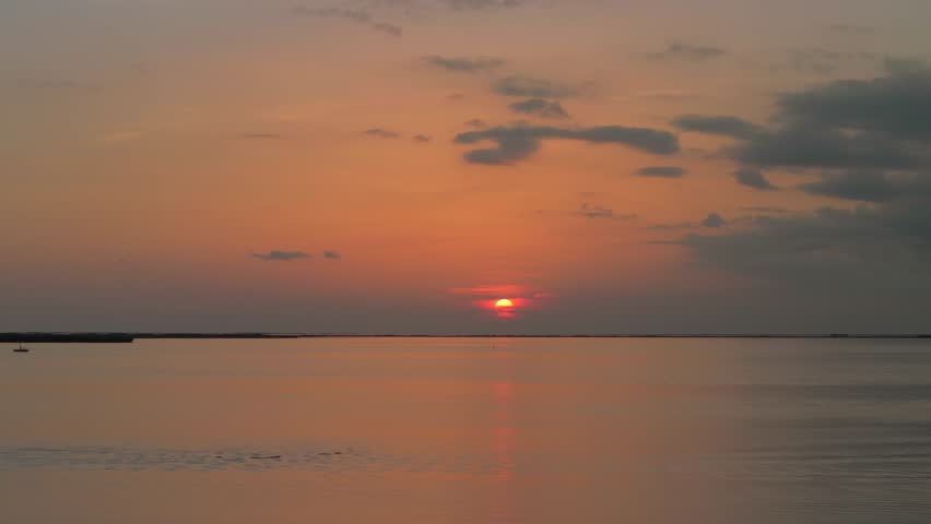 Aerial view of the sun setting over the ocean framed by silhouetted palm trees, casting an orange glow over the tranquil water, Key Largo, Florida, United States.