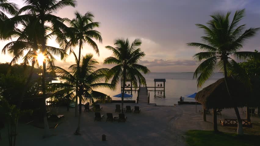 Aerial view of docks stretching into the calm ocean under a vibrant sunset sky, painting the water with hues of gold and purple, Key Largo, Florida, United States.