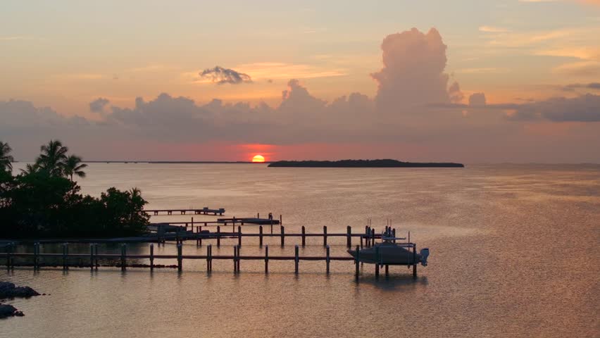 Aerial view of docks extending into serene water with boats, as the sun sets painting the sky with hues of orange and pink, Key Largo, Florida, United States.