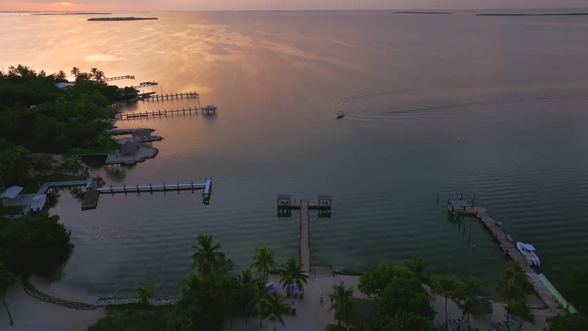Aerial view of piers stretching into the tranquil water, and a single boat sailing under a multicolored sunset sky, Key Largo, Florida, United States.
