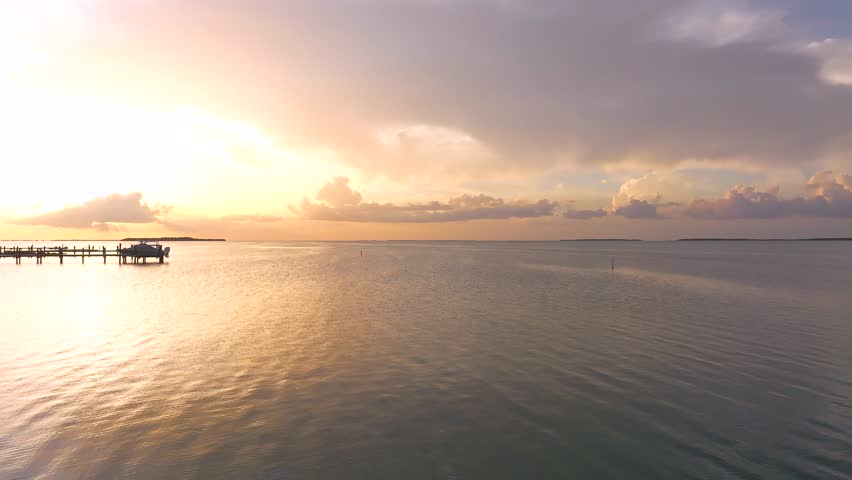 Aerial view of wooden docks with people relaxing under thatched roofs as the sun sets over the calm water, Key Largo, Florida, United States.