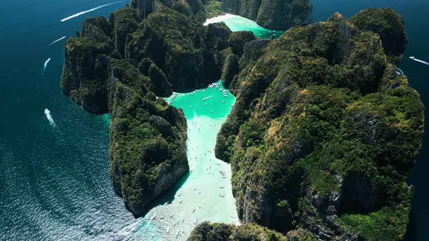 Aerial footage of vibrant turquoise lagoon and tour boats near Maya Bay, Thailand. Dramatic limestone cliffs and clear water create a perfect promo for exotic travel, tourism and luxury escapes.