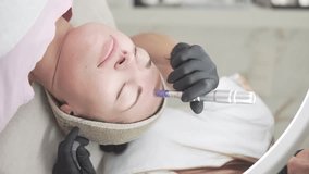 Vertical video. A woman is receiving a professional microneedling facial treatment at a beauty clinic. The cosmetologist, wearing gloves, uses a modern microneedling device on the clients forehead - Powered by Shutterstock - Get 15% off with code: PIKWIZARD15