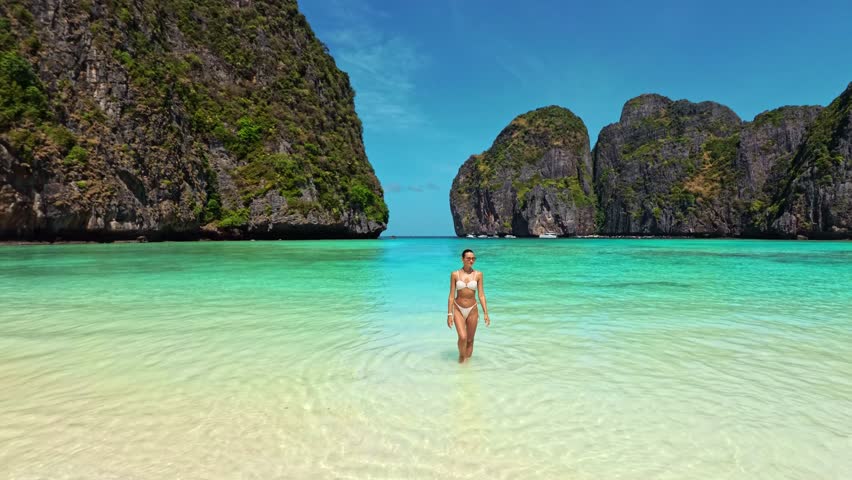 Model in white bikini walks out of turquoise water onto beach at Maya Bay, Thailand. Perfect for travel, summer, fashion and influencer campaigns. High quality tropical lifestyle footage.