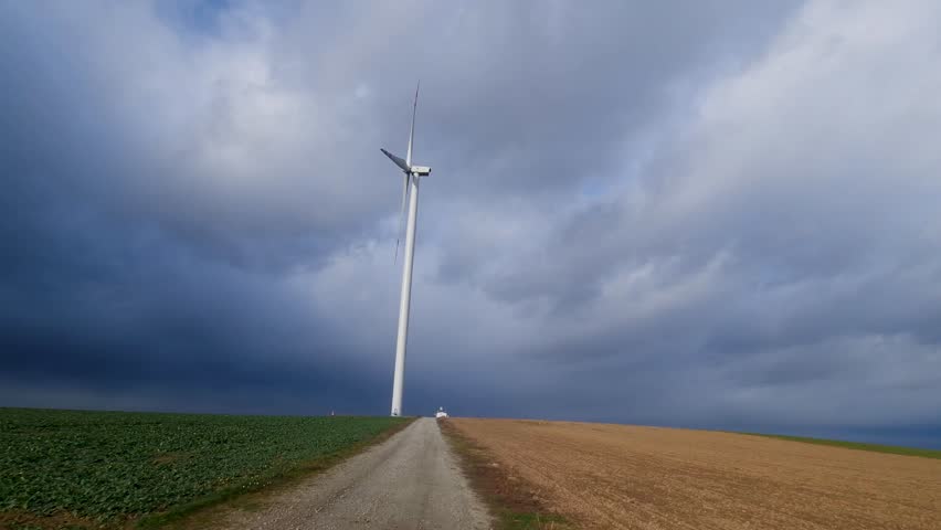 Large wind turbine stands tall in farm field under cloudy sky