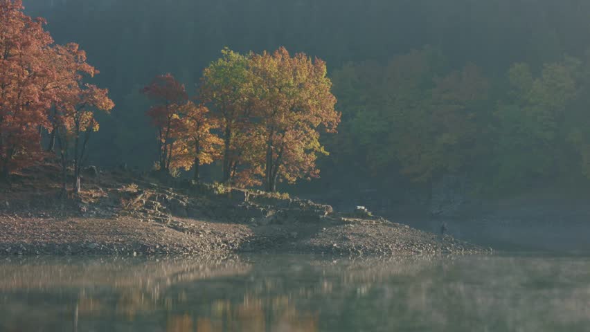 tranquil river landscape with fisherman in autumn sunrise