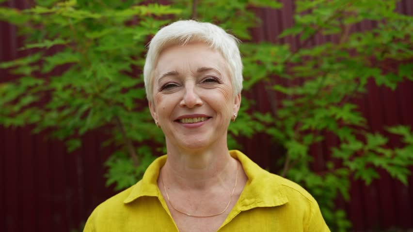 Closeup Portrait of Senior Woman Looking at Camera, Beautiful Face, Smiling. Elderly Lady with Natural Grey Hair, Blue Eyes. Abstract Beige Background, Tender and Soft Slow Motion