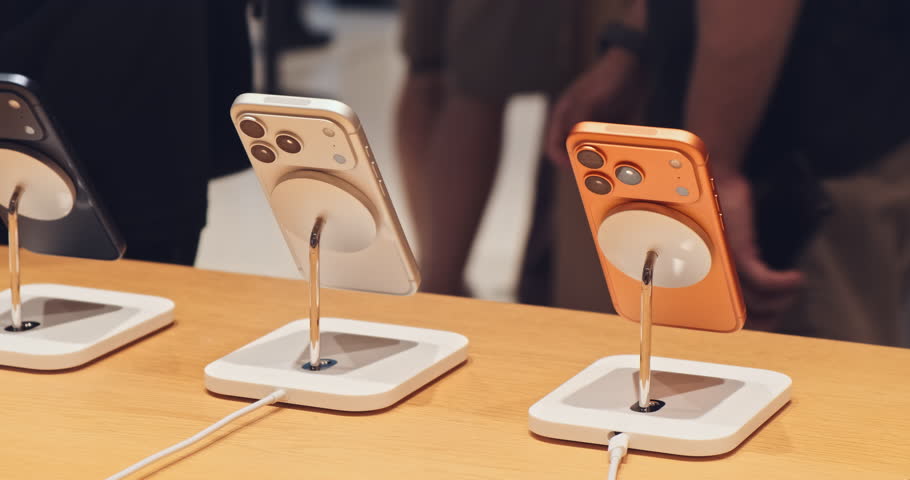 Phone smartphones on stands at Store retail table display, shoppers blurred. Clean showroom view of new phone lineup different colors, digital cameras. Innovation premium design