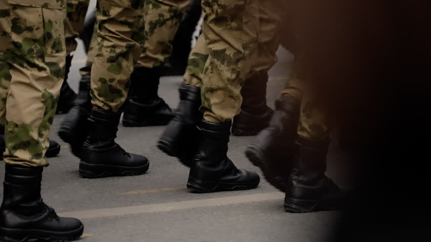 Close-up view of soldiers in camouflage uniforms marching in formation on a city street, black combat boots stepping in unison during a disciplined military parade or drill sequence