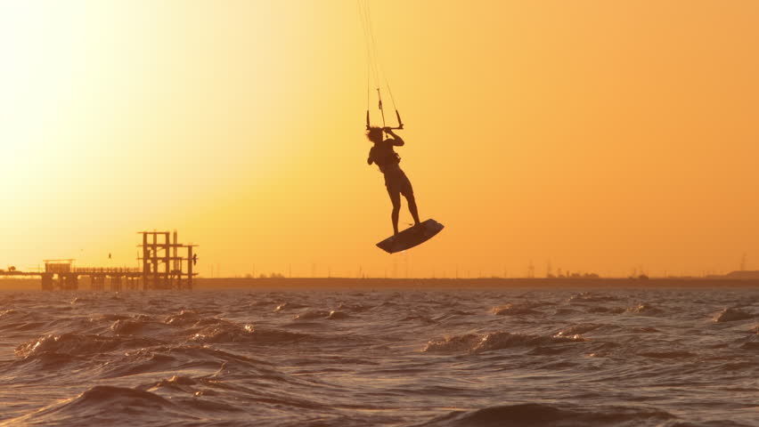 Extreme kitesurfer flying across ocean in golden sunset light creating water spray tropical holiday paradise lifestyle adventure freedom inspiration travel destination commercial background happiness