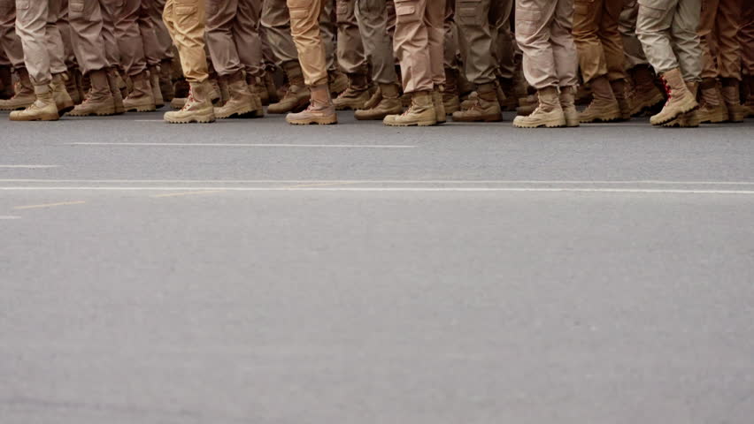 Close-up of uniformed soldiers marching in synchronized formation along an urban street, showcasing rugged boots, disciplined movement, and coordinated steps on parade