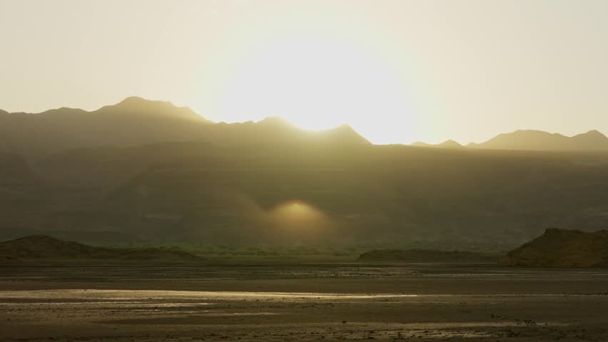 Warm sunlight during sunset or sunrise in Natron Lake in Tanzania Africa. Sun shining strong behind mountain range in savannah plains and high hills in nature reserve in safari vacation trip landscape