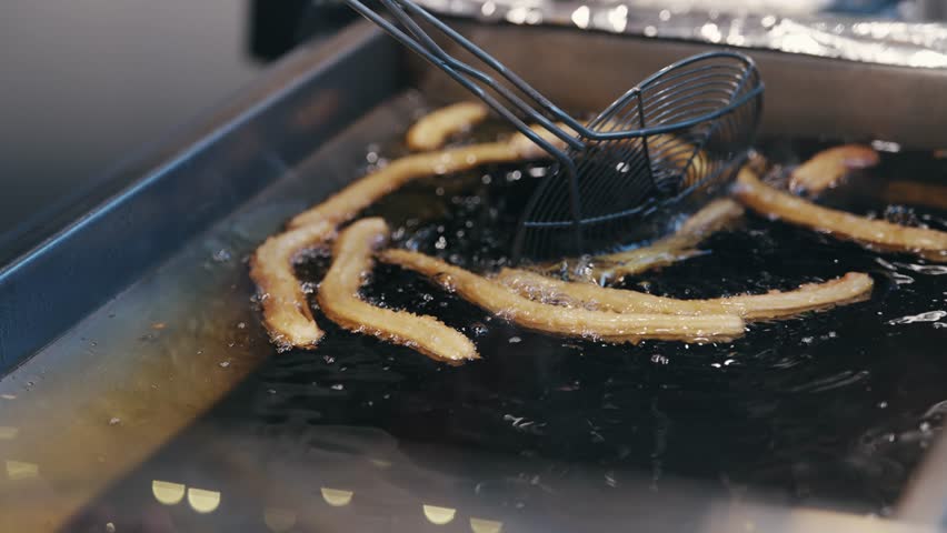 A person is frying churros in a pan fryer. The churros are in the process of being cooked and are surrounded by oil