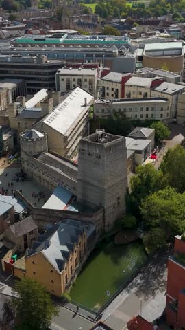 Vertical drone reversing from Oxford Castle and Prison, revealing Oxford’s skyline with historic spires, modern green rooftop architecture, and a blend of ancient and contemporary city landmarks.