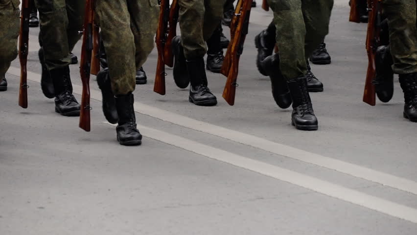 Close-up of soldiers in camouflage uniforms marching in formation during a military parade, rifles upright and boots striking asphalt in synchronized steps, emphasizing precision and ceremonial