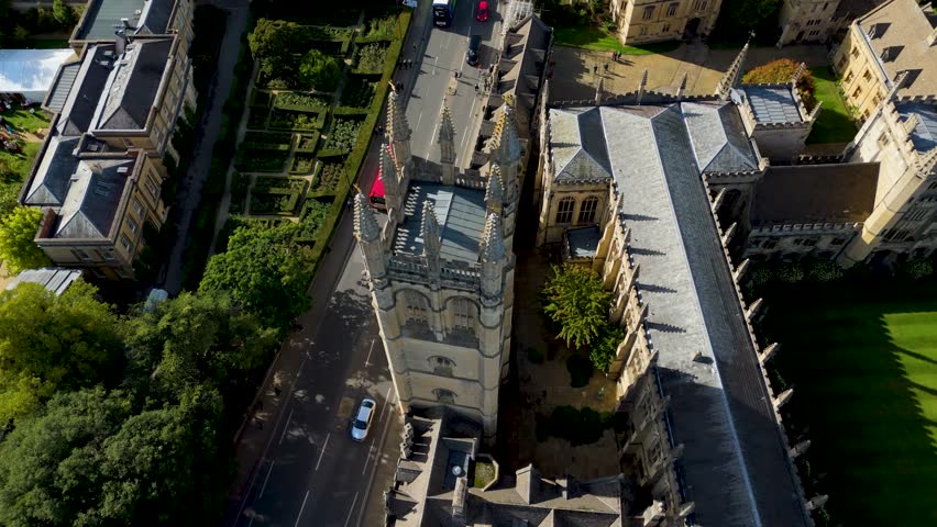 Aerial drone orbit of the Gothic tower at Magdalen College, Oxford, England. The shot begins angled at 45°, lowering as it circles, then rises to finish with a dramatic top-down view at about 80°.