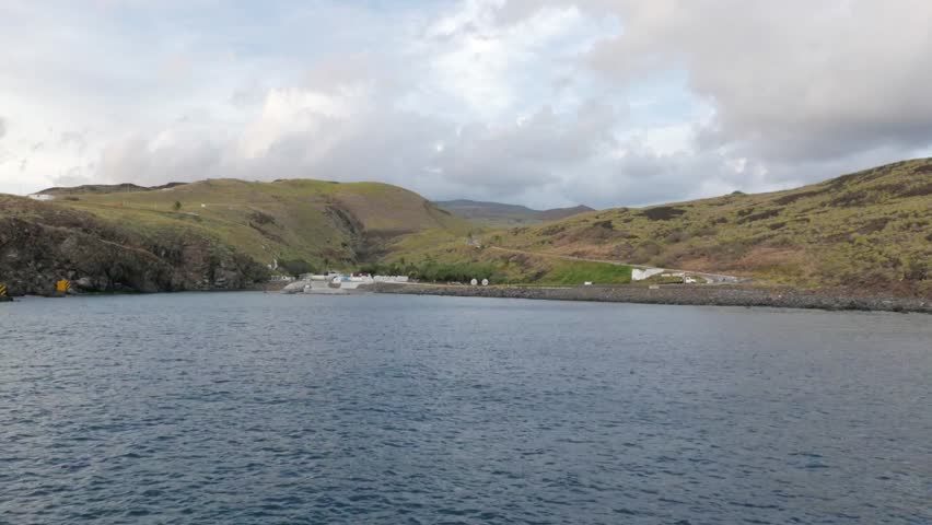 A tranquil view of a harbor with green hills under a cloudy sky