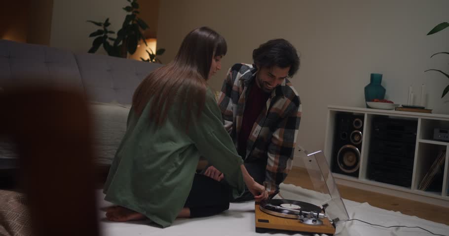 Boyfriend and girlfriend turn on vinyl record player and listen to vintage music during fun time and romantic vacation at home in cozy apartment at home in evening