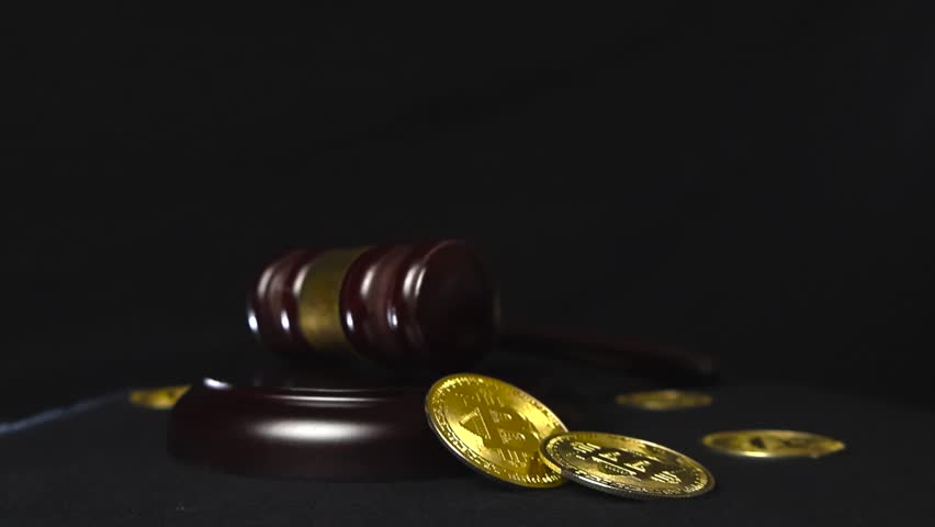 Close up slow motion footage of a justice court brown wooden hammer with bronze decoration slamming down and golden shiny and reflective bitcoin cryptocurrency coins around it flying and bouncing.