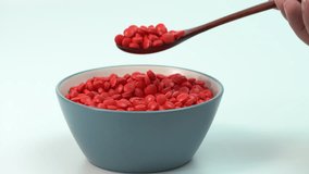 Hand holding wooden spoon scooping red pills from blue bowl, concept of daily medicine routine, pharmaceutical healthcare, overdose risk, and symbolic lifestyle image. - Powered by Shutterstock - Get 15% off with code: PIKWIZARD15