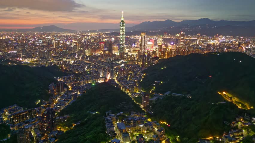 Aerial footage at nightfall above Downtown Taipei, vibrant capital city of Taiwan, with 101 Tower amid skyscrapers in XinYi Commercial District and buildings on the suburban hills under twilight sky