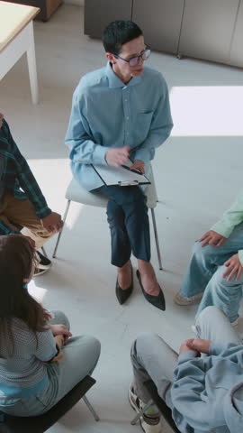 Vertical high angle shot of female counselor giving high-five to all participants of group school therapy session