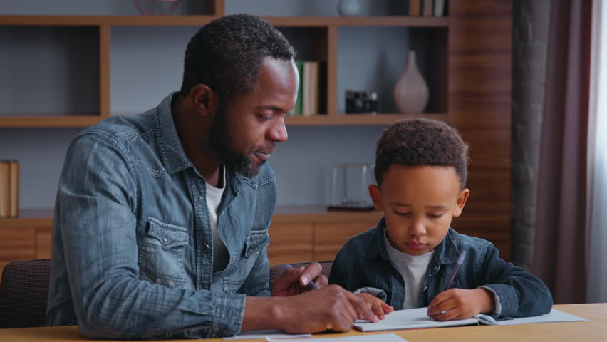 African American family dad assists son with learning teamwork lovely schoolboy with father writing homework at home child kid boy with parent tutor tutoring distant education concentration study