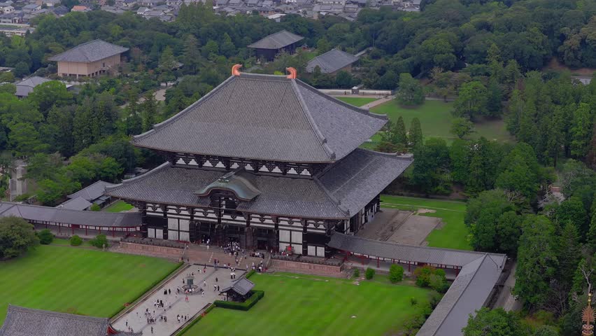 Aerial view of Todai ji Temple in Nara, Japan, showing its wooden architecture, lush greenery, a pond, and visitors walking on the temple grounds.