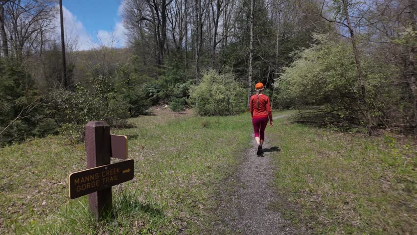 A mature woman enjoys hiking through scenic trails at Babcock State Park. She discovers beautiful waterfalls and lush greenery while exploring natures wonders.