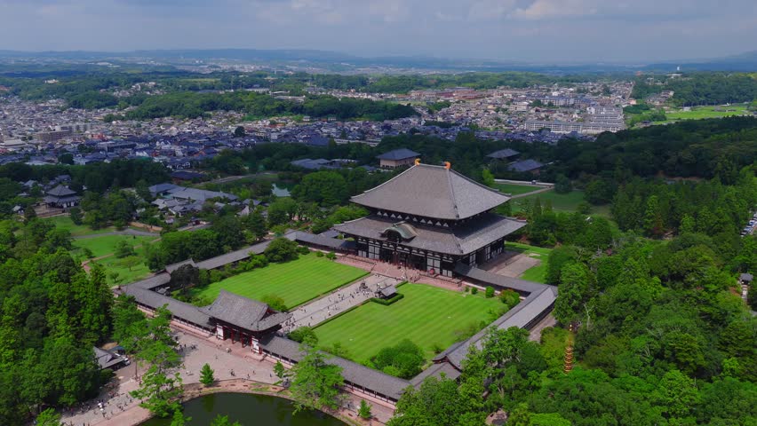 Aerial shot of Nara Todai ji Temple, showcasing its wooden structure, gardens, pond, pathways, and the urban sprawl of Nara in the background.