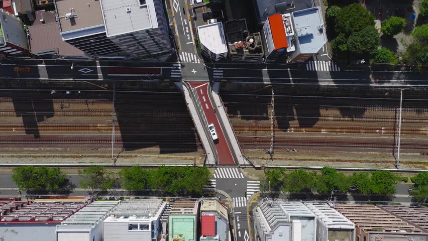Aerial view of Tokyo showing a railway with multiple tracks, a red pedestrian bridge, modern buildings, greenery, and organized roads with crosswalks.