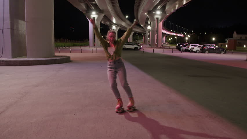 Young woman roller skater dances gliding under bridge at night