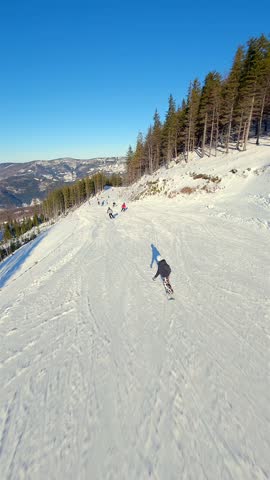 Smooth FPV drone flight over snowy ski slope with skiers enjoying winter sports in the mountains on clear sunny day. Perfect for themes of travel, lifestyle, holidays, and adventure.