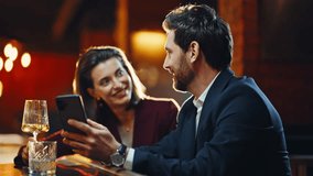 Flirting lady talking man at night celebration in pub lounge. Smiling couple enjoying beverages standing close to counter. Happy bar guests looking smartphone screen relaxing in glowing light lobby - Powered by Shutterstock - Get 15% off with code: PIKWIZARD15
