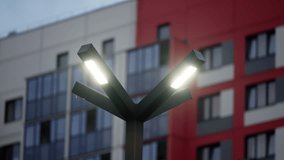 Three-armed LED streetlight glowing at dusk in front of a modern residential facade with red panels, glass balconies and windows, emphasizing contemporary urban architecture and geometric lines - Powered by Shutterstock - Get 15% off with code: PIKWIZARD15