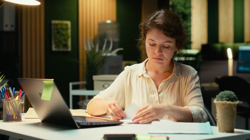 Livid businesswoman breaking a paper page after making a mistake, handwriting and notetaking in office after hours. Displeased impatient worker redoing the draft on a new sheet. Camera B.