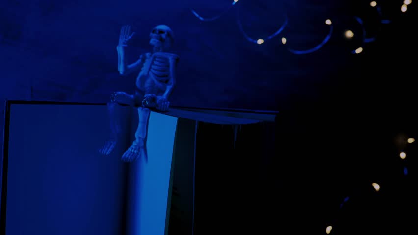 Halloween Book Mockup.Skeleton in the flickering light of garlands in blue light.Spooky Stories for Halloween. 4k footage