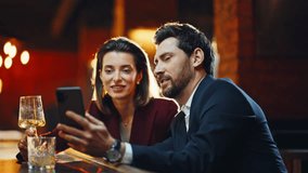 Elegant pair flirting bar counter staring smartphone together at evening closeup. Woman man in suits resting at modern pub using mobile phone. Luxury couple speaking in warm light environment place - Powered by Shutterstock - Get 15% off with code: PIKWIZARD15