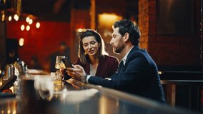 Man woman drinking alcohol sitting at modern pub counter using smartphone. Flirting people clinking glasses saying toasts at evening date atmosphere. Charming couple chatting in quiet stylish lounge - Powered by Shutterstock - Get 15% off with code: PIKWIZARD15