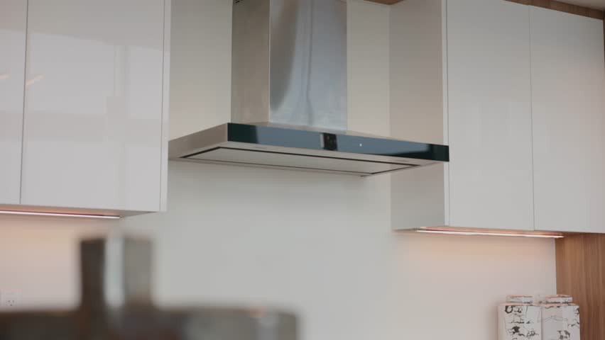 Modern kitchen with focus on cooking area. Silver range hood above stove top and white cabinets with lights under them. Clean countertop small with decorative item