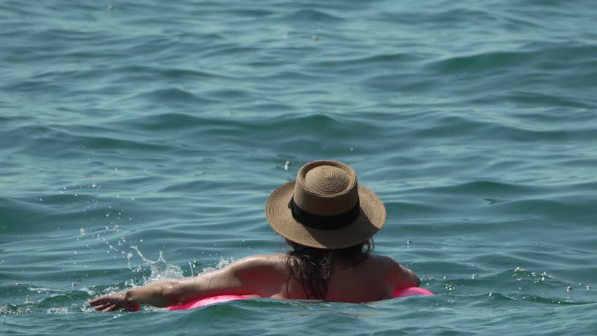Woman Floating Water, woman floats on pink ring in blue sea, splashing for summer relaxation.