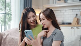 Two shocked young Asian women gossiping while looking at smartphone rest on sofa in living room.Friends surprised by news or intriguing social media content,showing negative emotions and reactions - Powered by Shutterstock - Get 15% off with code: PIKWIZARD15