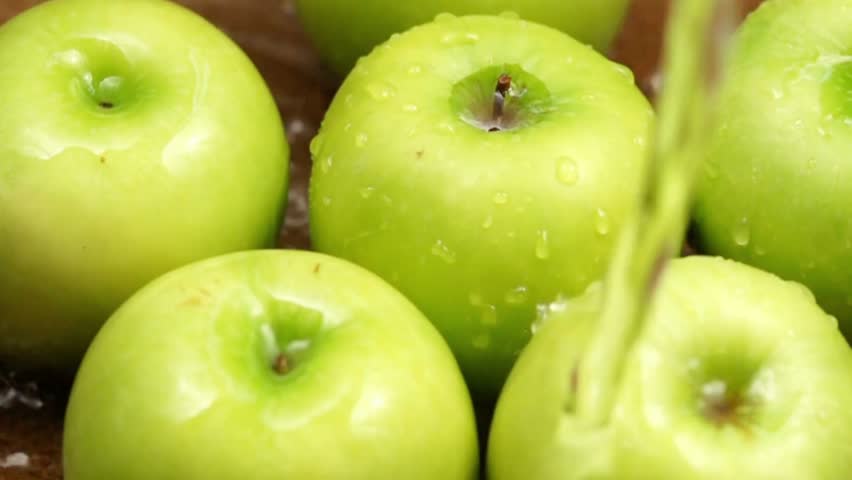 Fresh green apples are being washed with water, showing droplets on the skin