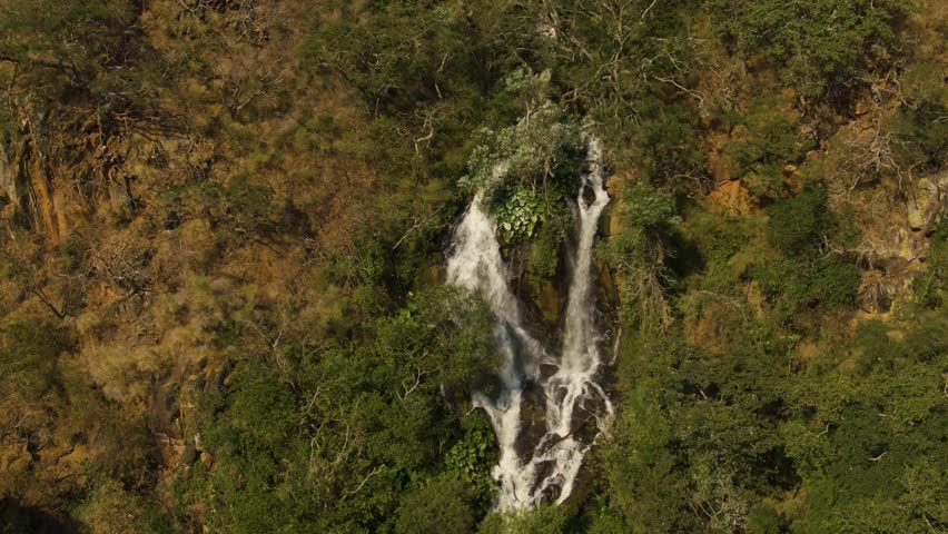 Zoom out drone view of thin waterfall cascading through dense forest on canyon slope in Vista Hermosa, Jalisco, Mexico
