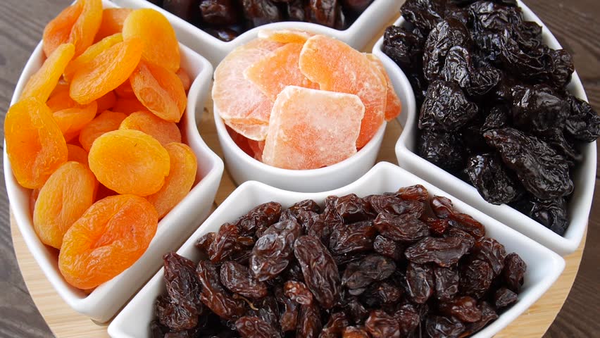 Top view of a rotating plate with a variety of dried fruits like apricots, prunes, dates, and raisins.