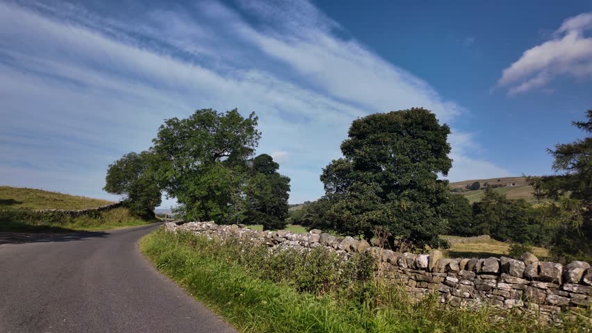 Quiet country lane in Weardale, County Durham on a sunny morning with stone walls and trees