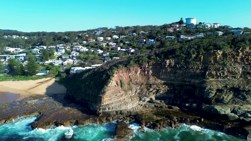 Drone aerial landscape pan around North Avoca rocky headland cliffs with surrounding bushland trees and residential housing along scenic coastline Central Coast NSW Australia nature tourism travel