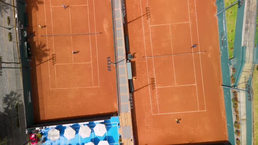 Sports facilities of Club Tenis Las Terrazas in Miraflores, Lima, people playing tennis on orange clay courts and an empty green soccer field - top-down aerial flyover